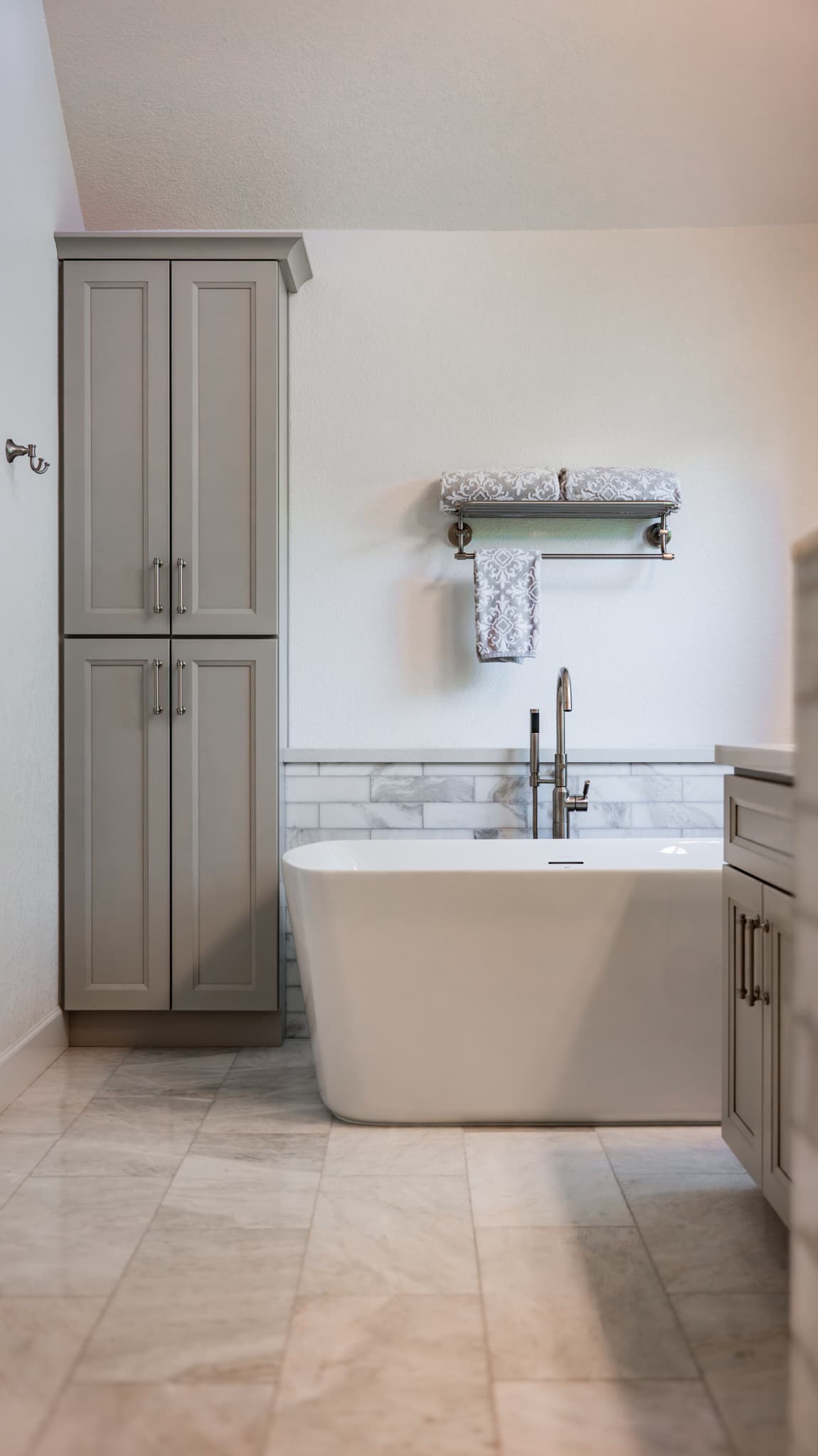 Bathroom Remodel in Sacramento — freestanding tub, linen tower, shaker cabinets, natural-stone backsplash, marble tile flooring